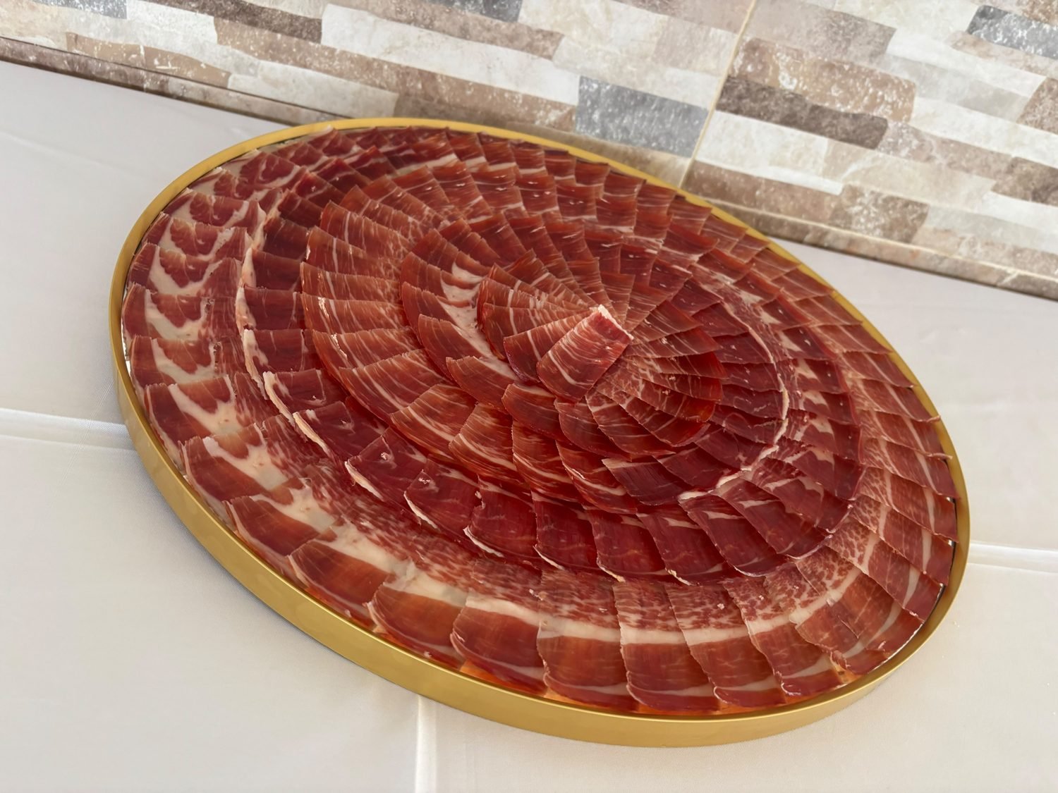 Bandeja circular de borde dorado cubierta con hileras de lonchas de jamón ibérico