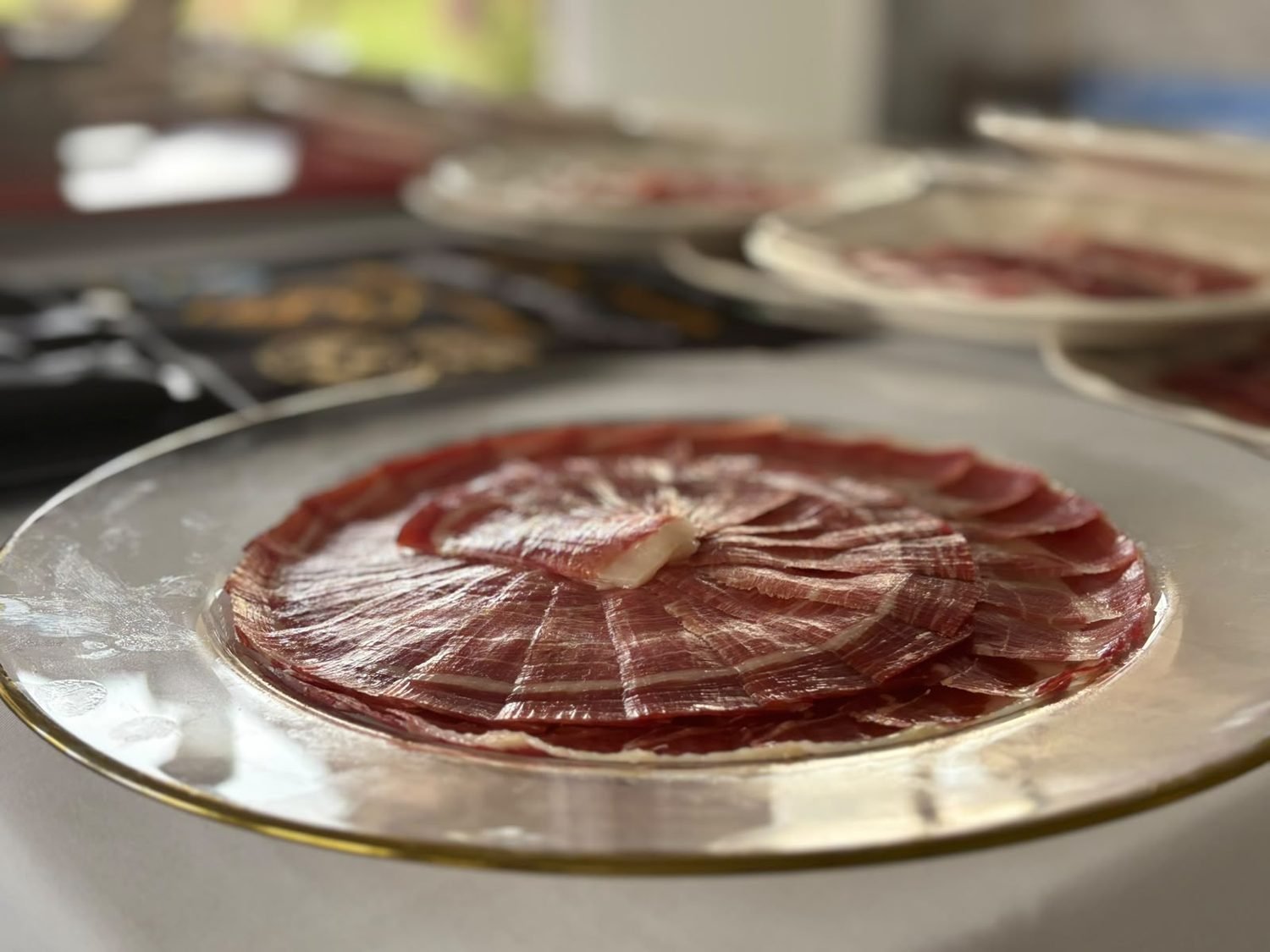 Plato de cristal con borde dorado y un espiral delicado de jamón ibérico
