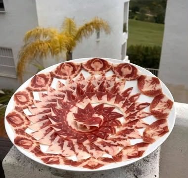 Plato blanco con lonchas de jamón veteado colocadas en círculos decorativos