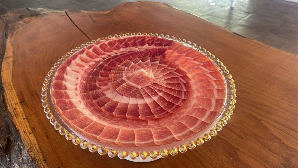 Plato con lonchas de jamón ibérico en espiral concéntrica sobre una mesa de madera de una sola pieza