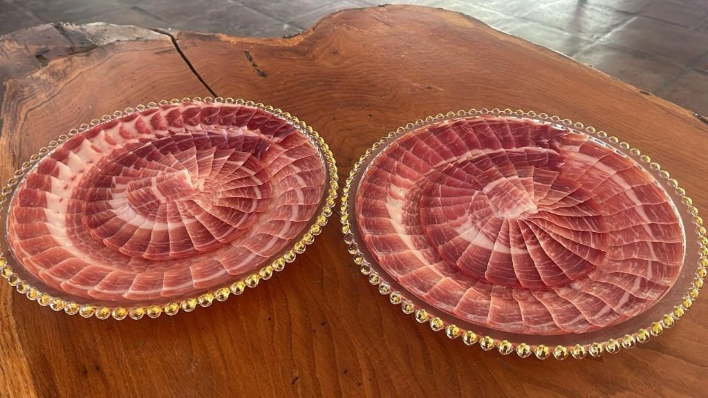 Dos platos de cristal con rosetas de lonchas de jamón ibérico presentados juntos sobre una mesa de madera